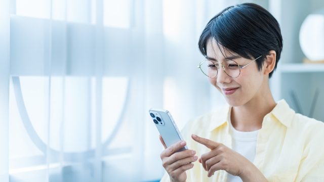 眼鏡をかけた女性がスマホで調べものをしている写真。就労移行支援を事業所をインターネットで検索している。見学や相談会も確認。