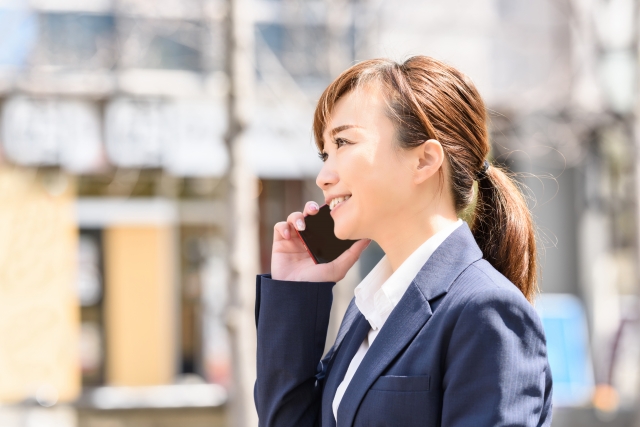 屋外で笑顔で電話で話をしている女性の写真。就労移行支援の見学の予約をしているようす。