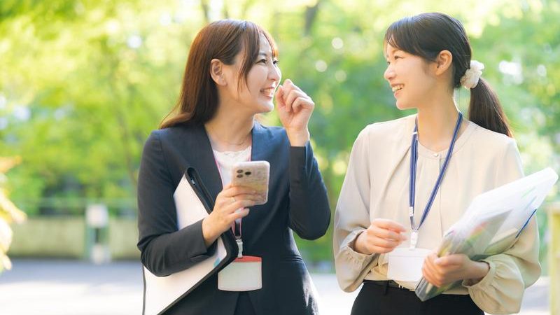 仕事中楽しく会話をする女性2人の写真。就労移行支援を利用して一般就労を実現しよう。