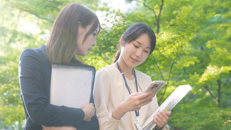 相談しながら新緑の中を歩く女性２人の写真。定着支援を受けると利用者は体調面や生活面の不安も解消でき、安心感を持って働き続けることができる。