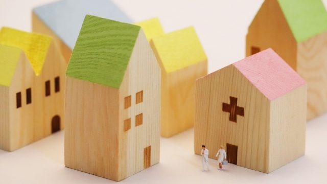 就労選択支援事業者はハローワークへの訪問等や地域における就労支援に係る社会資源との関係機関連携が求められる。家や病院をモチーフにした街並みの写真。