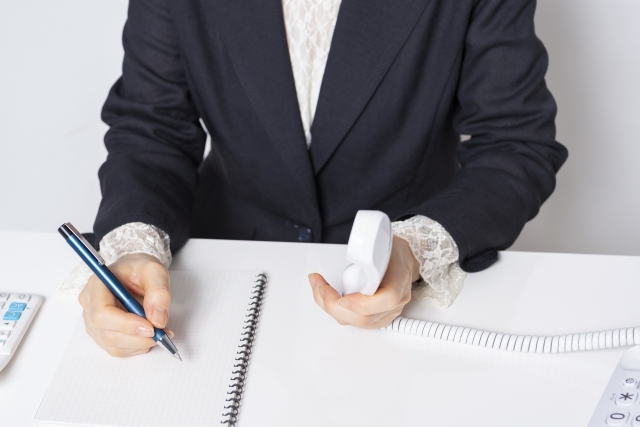 メモをとりながら受話器を持つ手元の画像