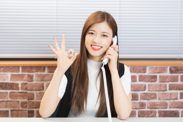 電話をしながらOKマークを出している女性の画像