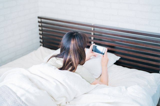 ベッドでスマホを触る女性の画像